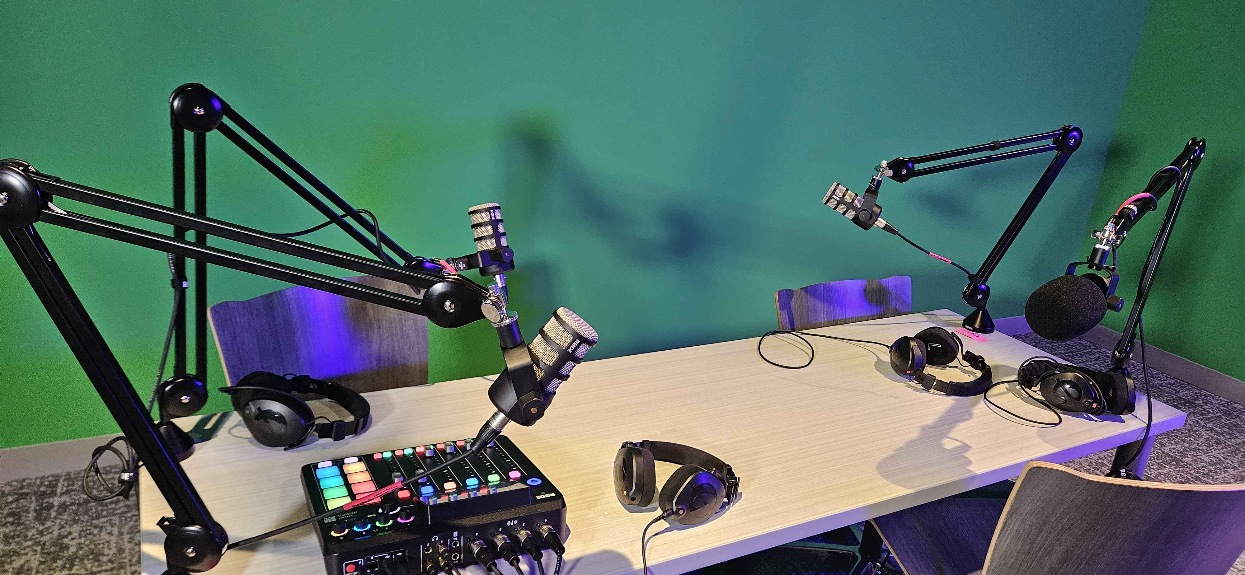 Studio A Podcasting Table complete with the RodeCaster Pro II Mixing Board, 4 headphones and microphones in front of the Greenscreen wall.